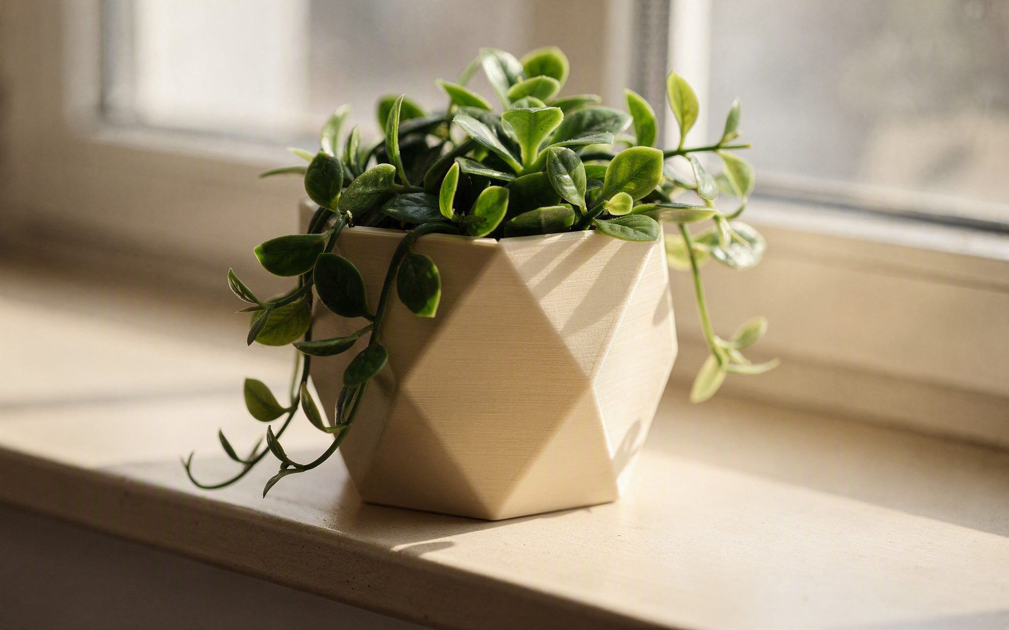 A geometric 3D-printed planter with a trailing plant on a windowsill