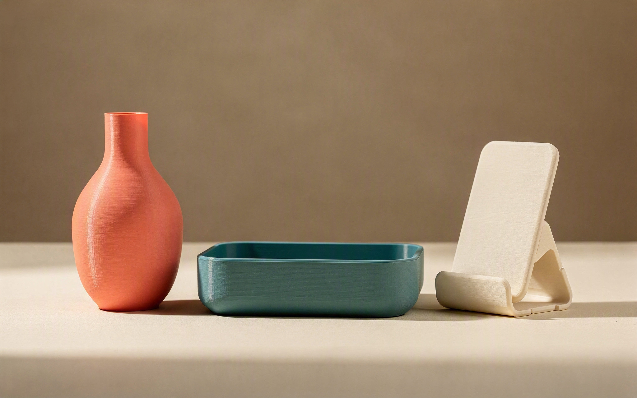 Three 3D-printed products from one product line — a vase, a desk tray and a phone stand